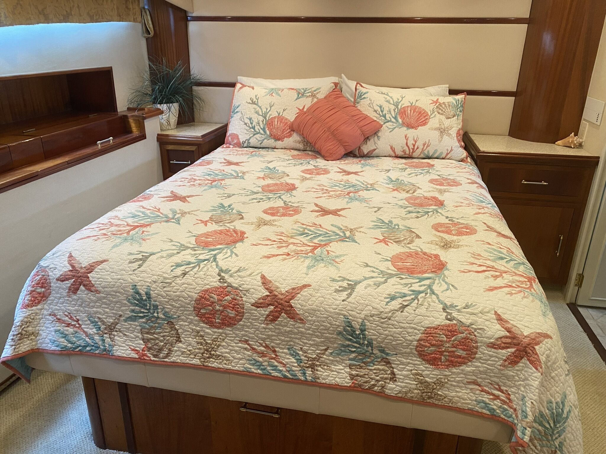 Ein Schlafzimmer mit einer floralen Steude, einem Holzkopfende, Nachttischen und einem Beistelltisch mit einer Pflanze.