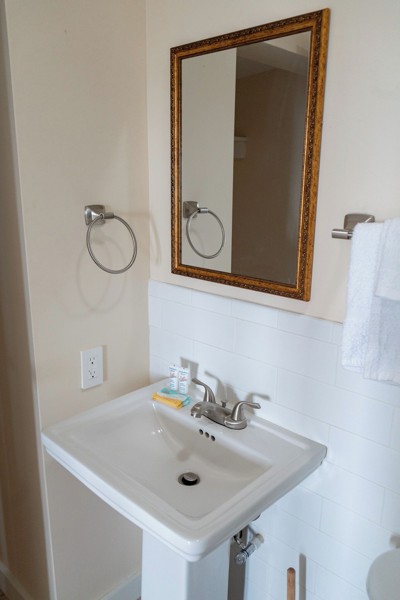 A bathroom with a white sink, a gold-framed mirror, and a towel ring.