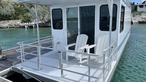 Un barco blanco con cubierta protegida, sillas blancas y un ventanal pequeño.