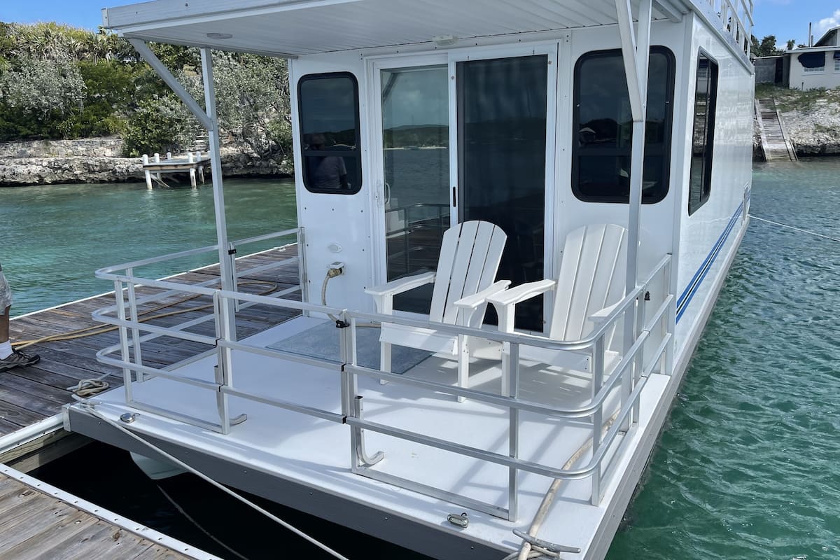 Un barco blanco con cubierta protegida, sillas blancas y un ventanal pequeño.