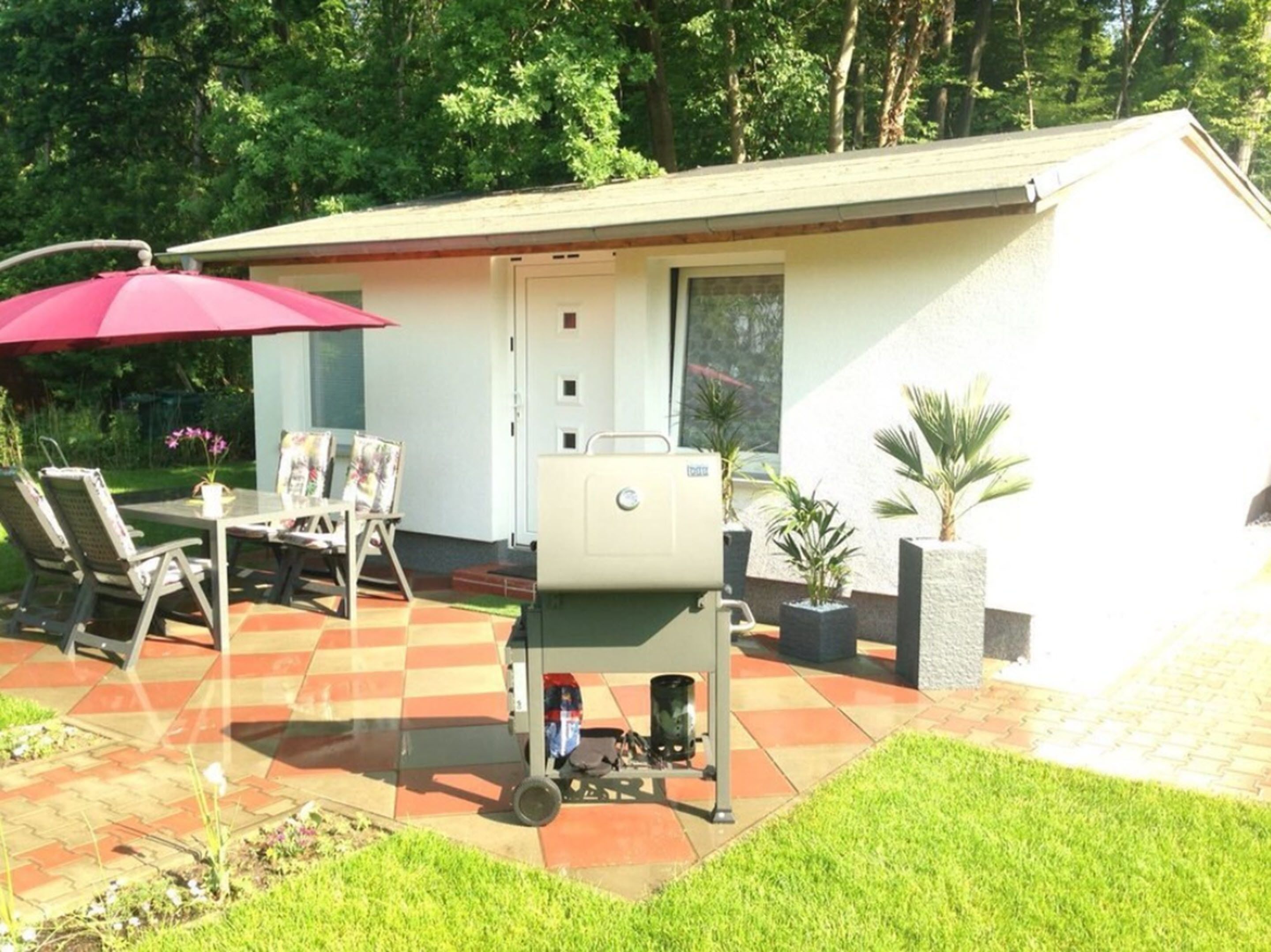 Un patio con una parrilla, mobiliario exterior y un área cubierta con un paraguas rojo.
