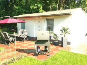 A patio with a grill, outdoor seating, and a covered area with a red umbrella. - Kleines Ferienhaus (Berlin)