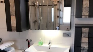 A modern bathroom with a large mirror, a glass shower enclosure, a white sink, and black cabinets. - Kleines Ferienhaus (Berlin)