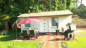A single-story house with a patio area, a dining table with chairs, and a red umbrella. - Kleines Ferienhaus (Berlin)