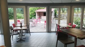 Un restaurant doté d’une salle à manger intérieure et d’une terrasse, de grandes fenêtres et offrant une vue sur l’extérieur.