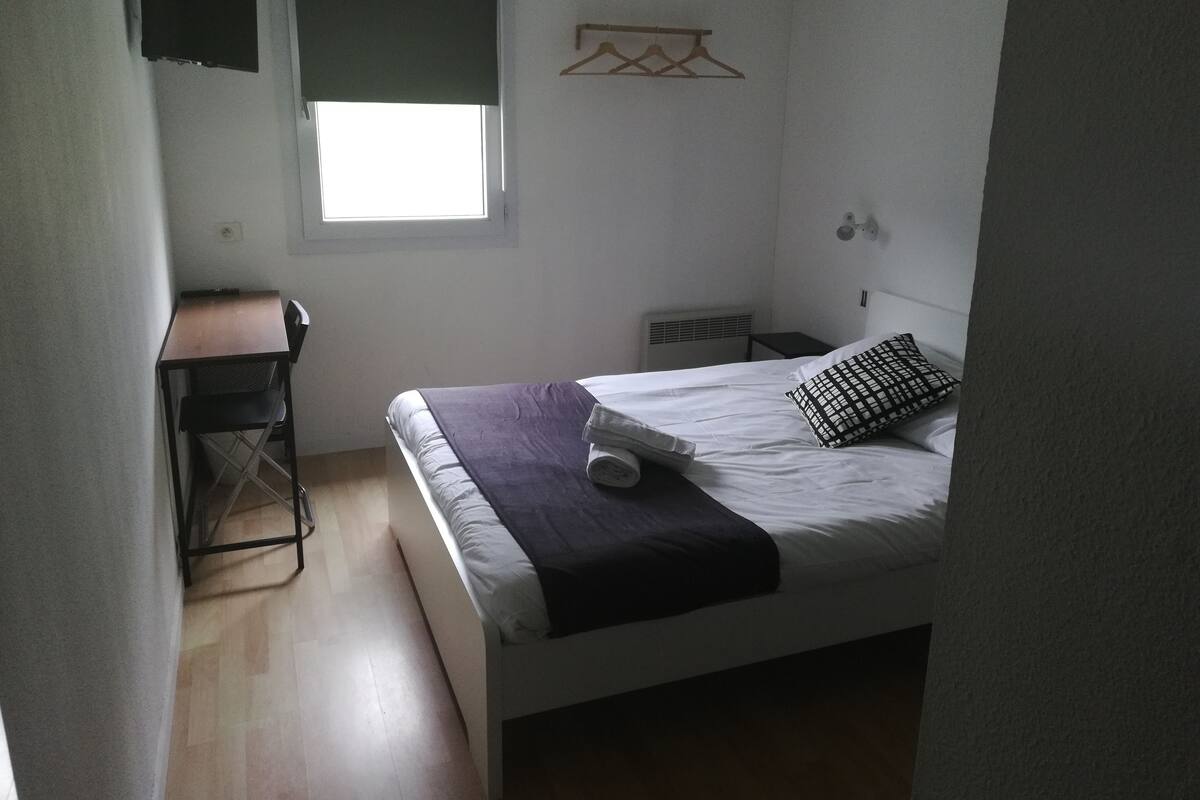 Una habitación pequeña y poco amueblada con una cama, un escritorio y una ventana.