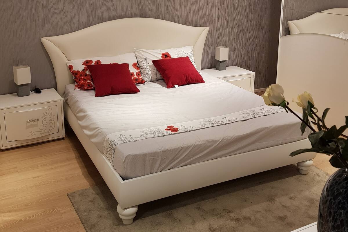 A modern bedroom with a large bed, two nightstands, a bedside table, and a vase with flowers.