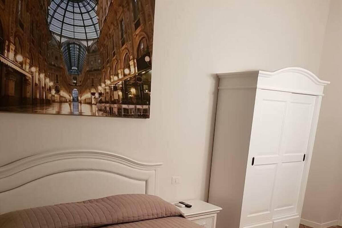 A bedroom with a bed, a nightstand, a wardrobe, and a painting of a building.