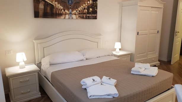 A neatly made bed with a quilted cover, two bedside lamps, a nightstand with a drawer, and a folded towel on the bed. - Villa Gatti (Milan)