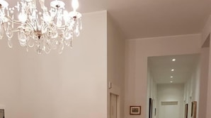 A dining area with a wooden table and chairs, a chandelier, and a patterned rug. - Villa Gatti (Milan)