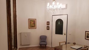 A dining area with a wooden table, chairs, a chandelier, a radiator, and framed pictures on the wall. - Villa Gatti (Milan)
