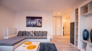 Una sala moderna con un sofá modular, una mesa de centro con detalles amarillos, un cuadro de una vista urbana y una estantería empotrada.