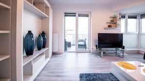 Un salón moderno con televisor, estanterías y puerta corrediza de vidrio a un balcón.