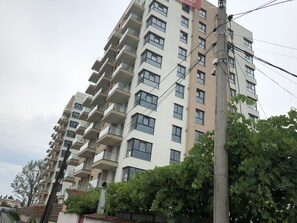 A multi-story residential building with balconies, a visible utility pole, and lush green foliage in the foreground.