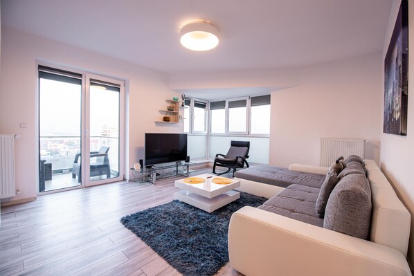A modern living room with a sofa, a coffee table, a TV, and a large window with a view.