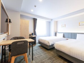 Habitación de hotel con escritorio, dos camas, armario, ventana con cortinas e iluminación en el techo.