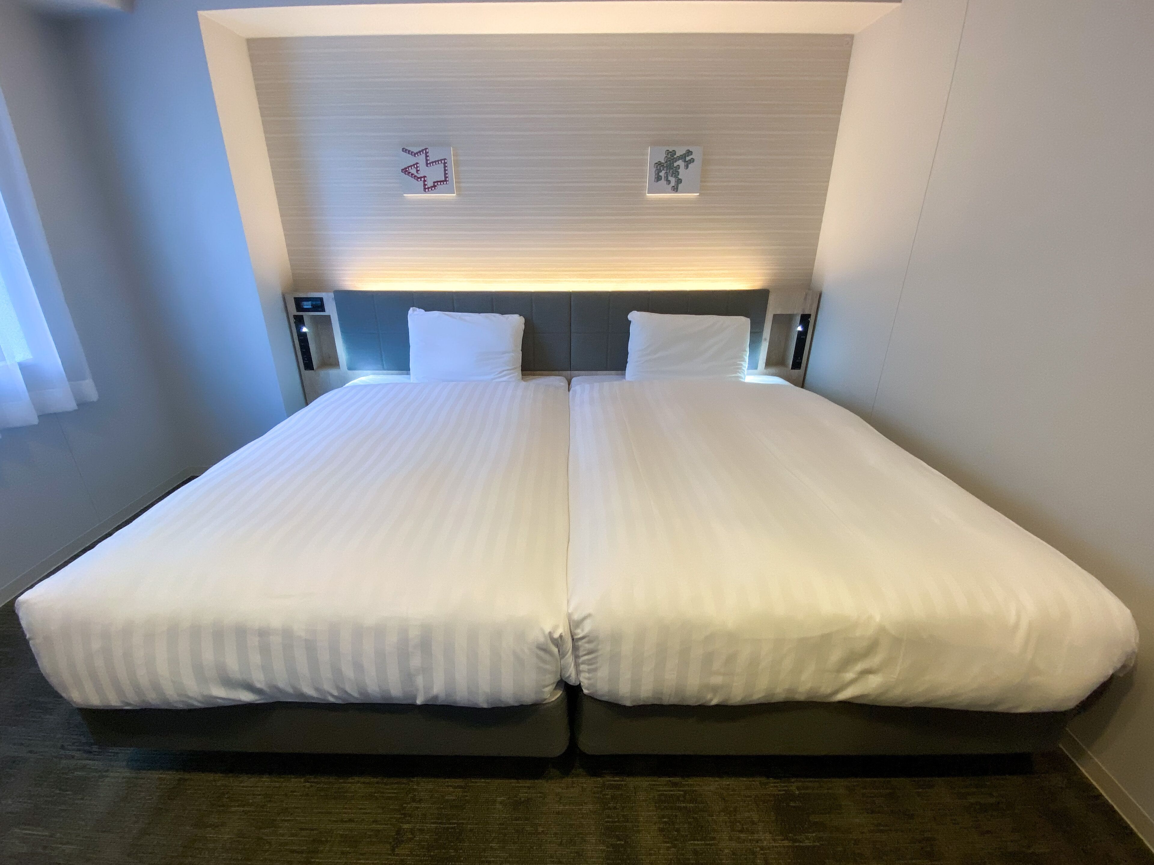 A double bed with two pillows, a headboard with a light fixture, and a small wall decoration.