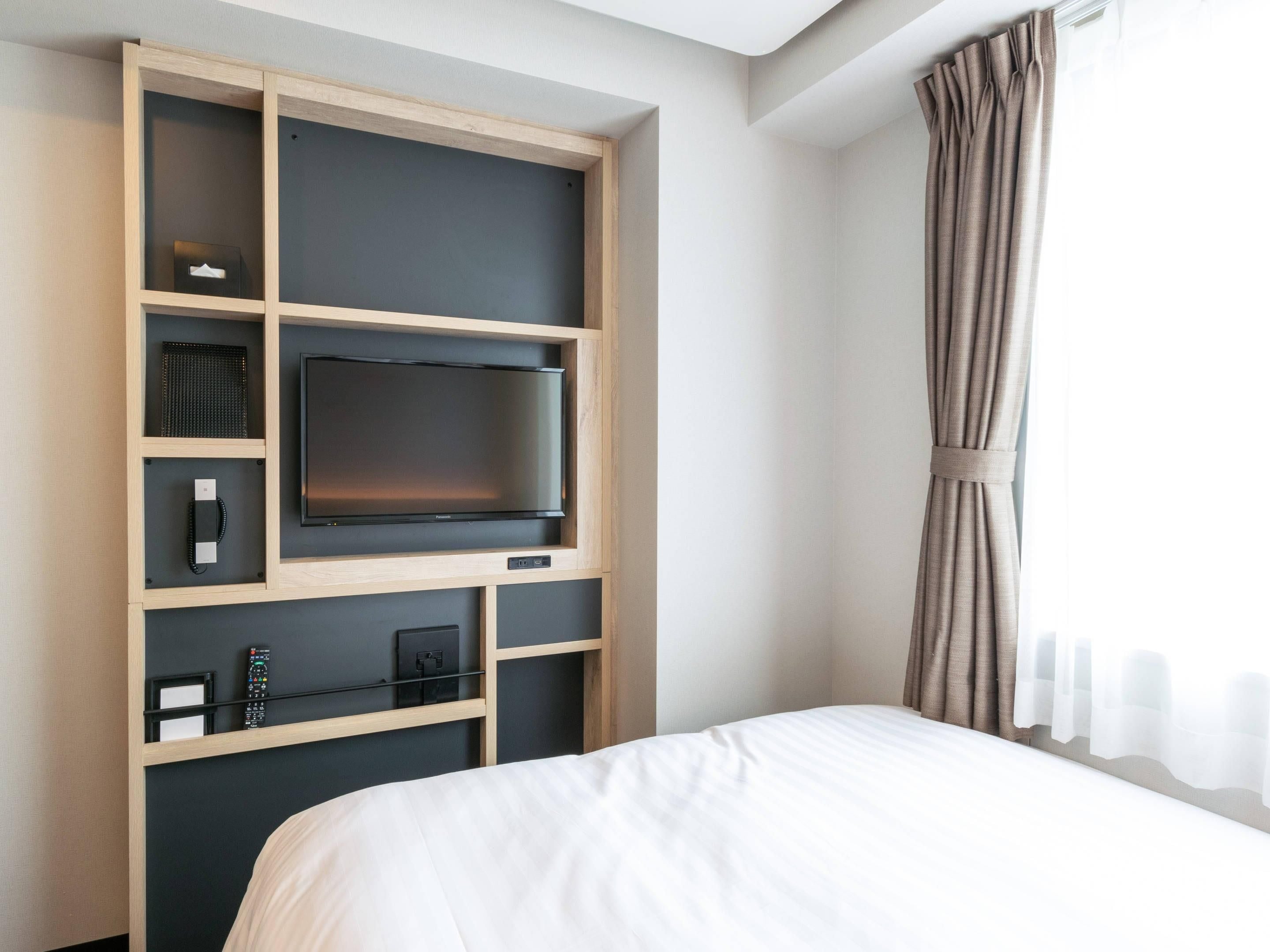 Habitación de hotel con cama, televisor montado en un estante de madera, teléfono y control remoto.