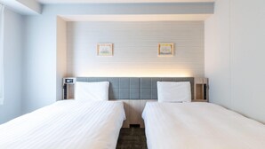 Habitació d'hotel amb dos llits individuals, un capçal de llit amb plafó d'il·luminació i dos quadres a la paret.