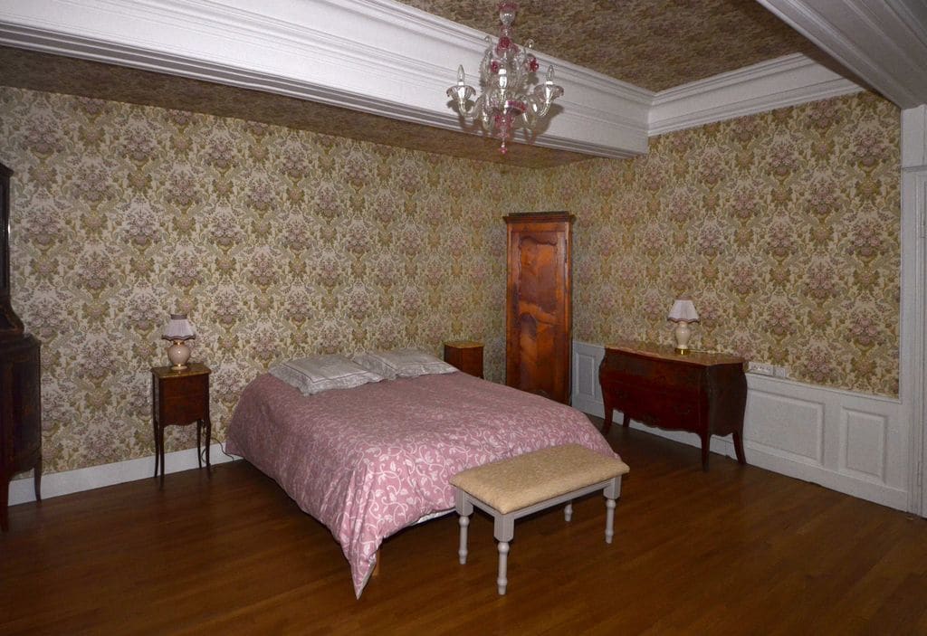 A bedroom with a wooden bed, a bench, two nightstands, a dresser, and a chandelier.
