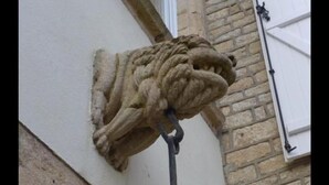 Escultura de cabeza de león de piedra adosada a la pared exterior de un edificio.