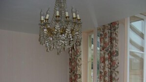 Comedor con mantel rosa, sillas de madera, lámpara de araña y cortinas con motivos florales.