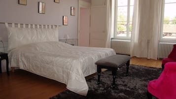 A bedroom with a large bed, a bench, a nightstand, a window with curtains, and a door.