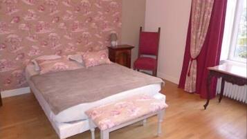 Quarto com cama, cadeira, mesa e janela com cortinas.