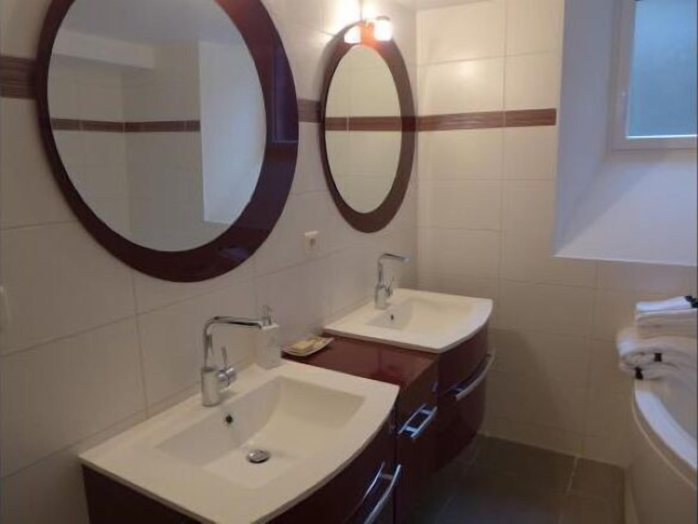 Une salle de bain avec deux lavabos, chacun étant surmonté d’un miroir. Il y a des placards sous les lavabos.