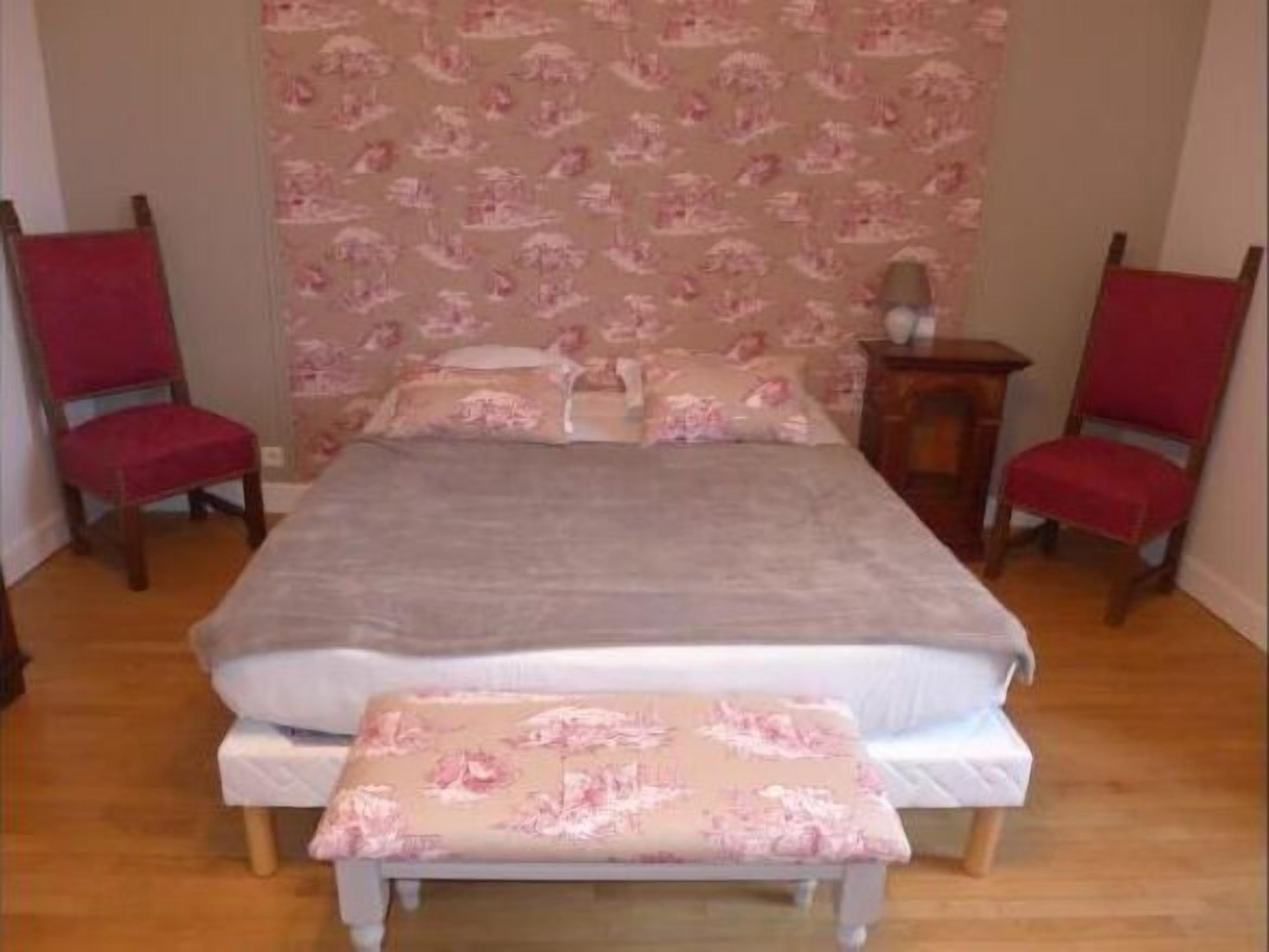 Une chambre à coucher avec un lit, deux chaises rouges, une table de chevet en bois et un papier peint à motifs floraux.