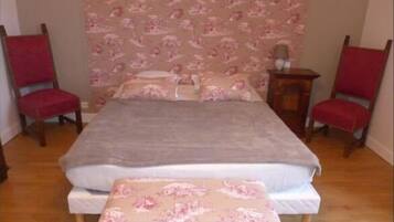 Une chambre à coucher avec un lit, deux chaises rouges, une table de chevet en bois et un papier peint à motifs floraux.