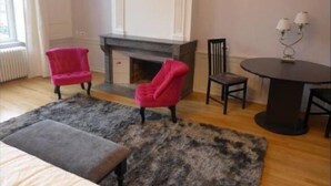 Una habitación con chimenea, dos sillones rosas, una mesa redonda con dos lámparas y una alfombra gris.
