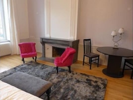 Una habitación con chimenea, dos sillones rosas, una mesa redonda con dos lámparas y una alfombra gris.