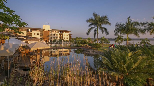 A resort with a swimming pool, palm trees, and a building with multiple balconies. - Life Resort Hplus Long Stay (Brasília)