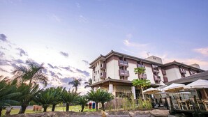 A multi-story hotel with balconies, a covered outdoor seating area, and palm trees. - Life Resort Hplus Long Stay (Brasília)