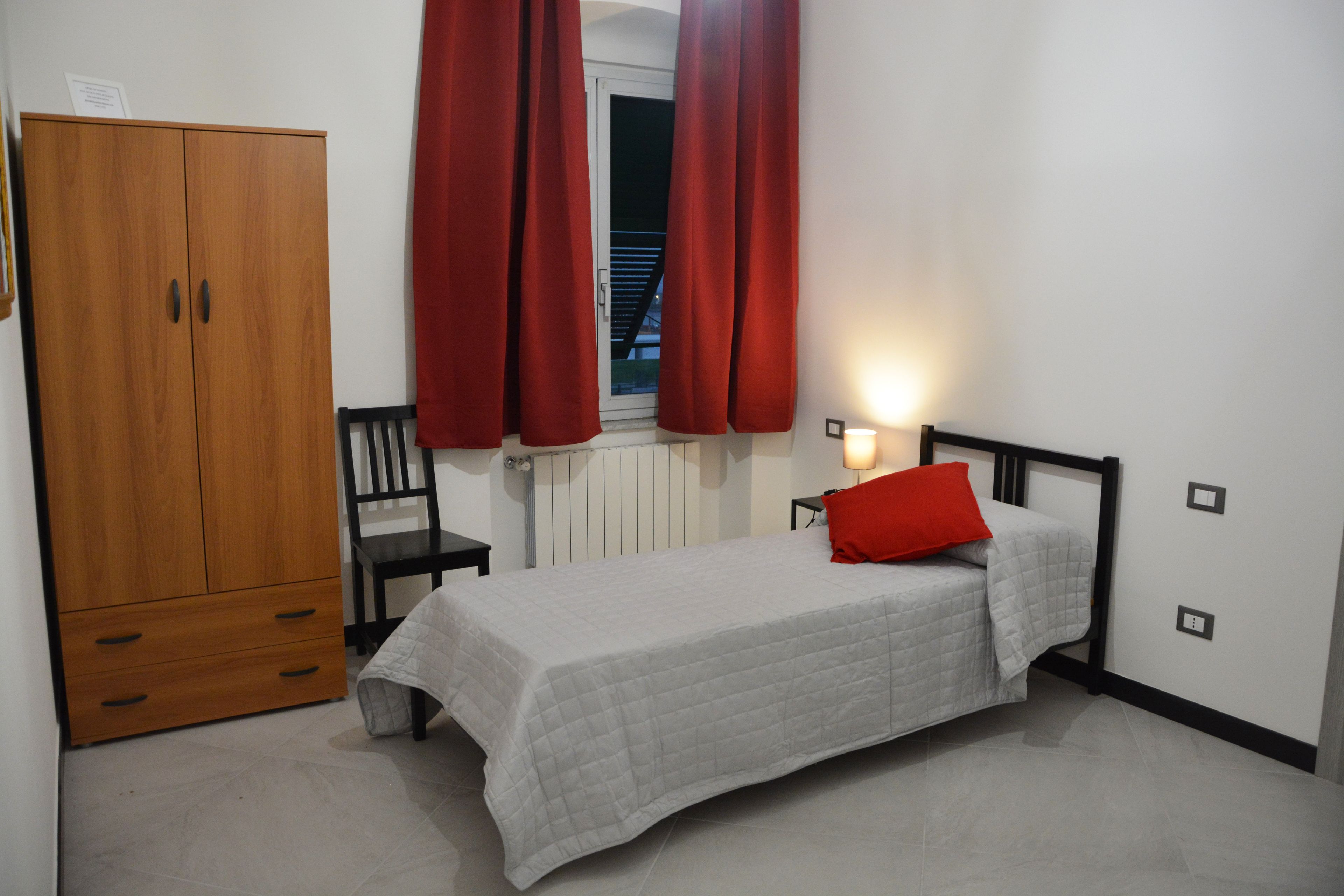 Ein Schlafzimmer mit Bett, Kleiderschrank, Stuhl und einem Fenster mit Vorhängen.