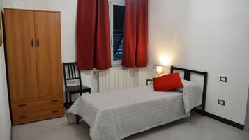 Ein Schlafzimmer mit Bett, Kleiderschrank, Stuhl und einem Fenster mit Vorhängen.