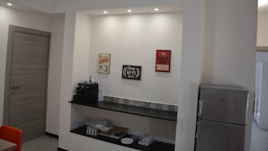 A kitchen with a refrigerator, a coffee machine, and a shelf with dishes. There are three signs on the wall, one of which says "Free Wi-Fi here." - Casa dei Nonni (Genoa)