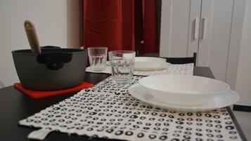 Une table dressée avec une nappe à motifs, une assiette blanche, un verre et un pot muni d’une anse.
