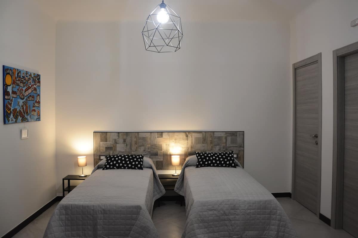 A bedroom with two beds, a geometric pendant light, a wooden headboard, and a nightstand with a lamp.