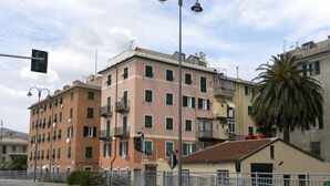A multi-story building with balconies, a street with a pedestrian crossing, and a palm tree. - Casa dei Nonni (Genoa)