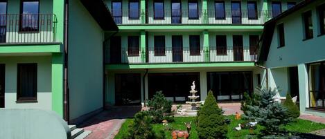 Un edificio de dos pisos con fachada verde, varios balcones y un patio central con una fuente y estatuas.