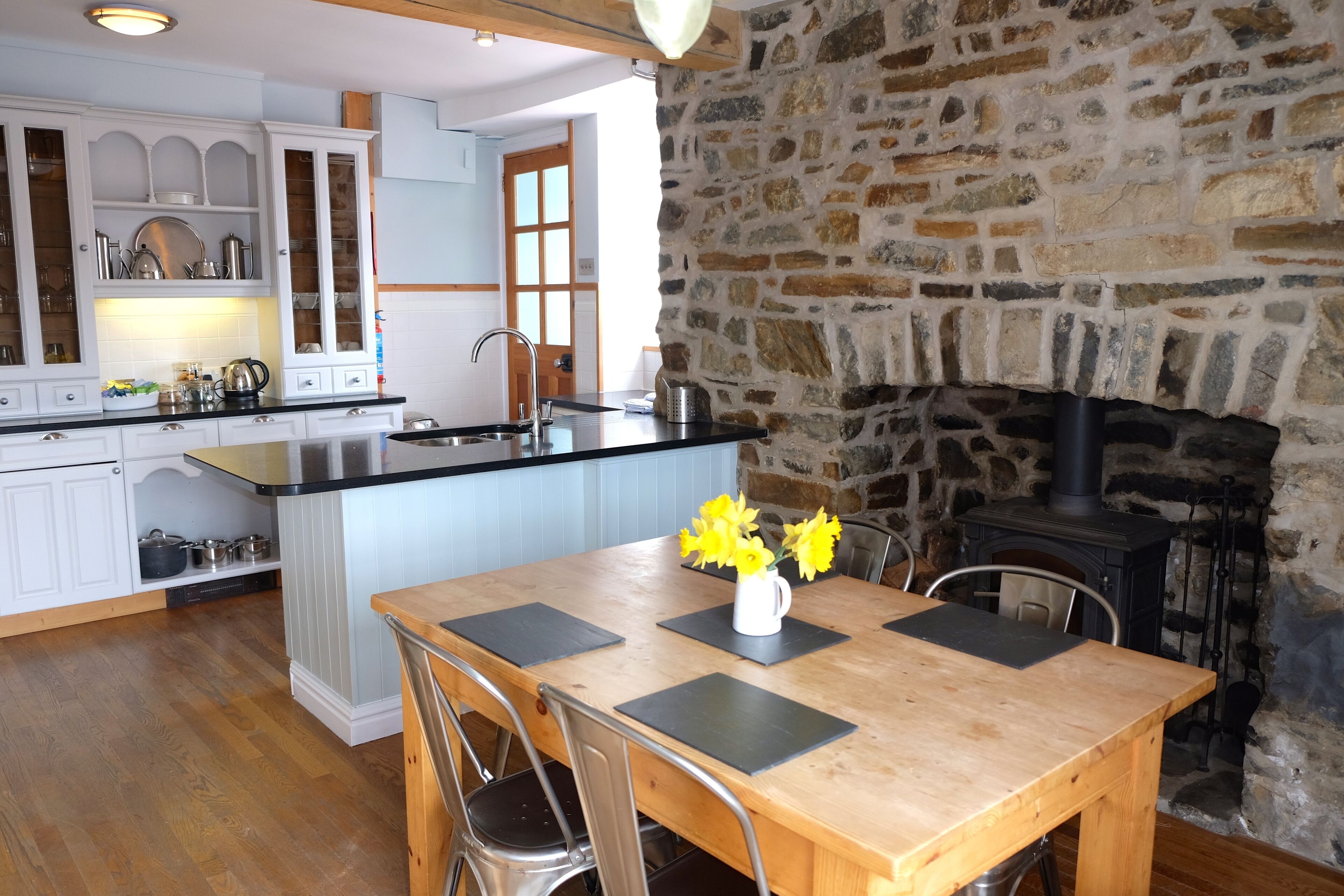 A kitchen with white cabinets, a stone wall, a fireplace, and a dining area with a table and chairs.