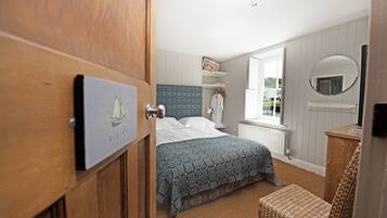 Un dormitorio con cama, una puerta de madera, una ventana, un espejo y una repisa con una toalla.