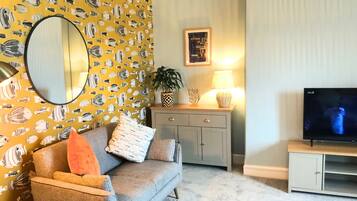 A living room with a sofa, a TV, a lamp, and a wall with fish patterns.