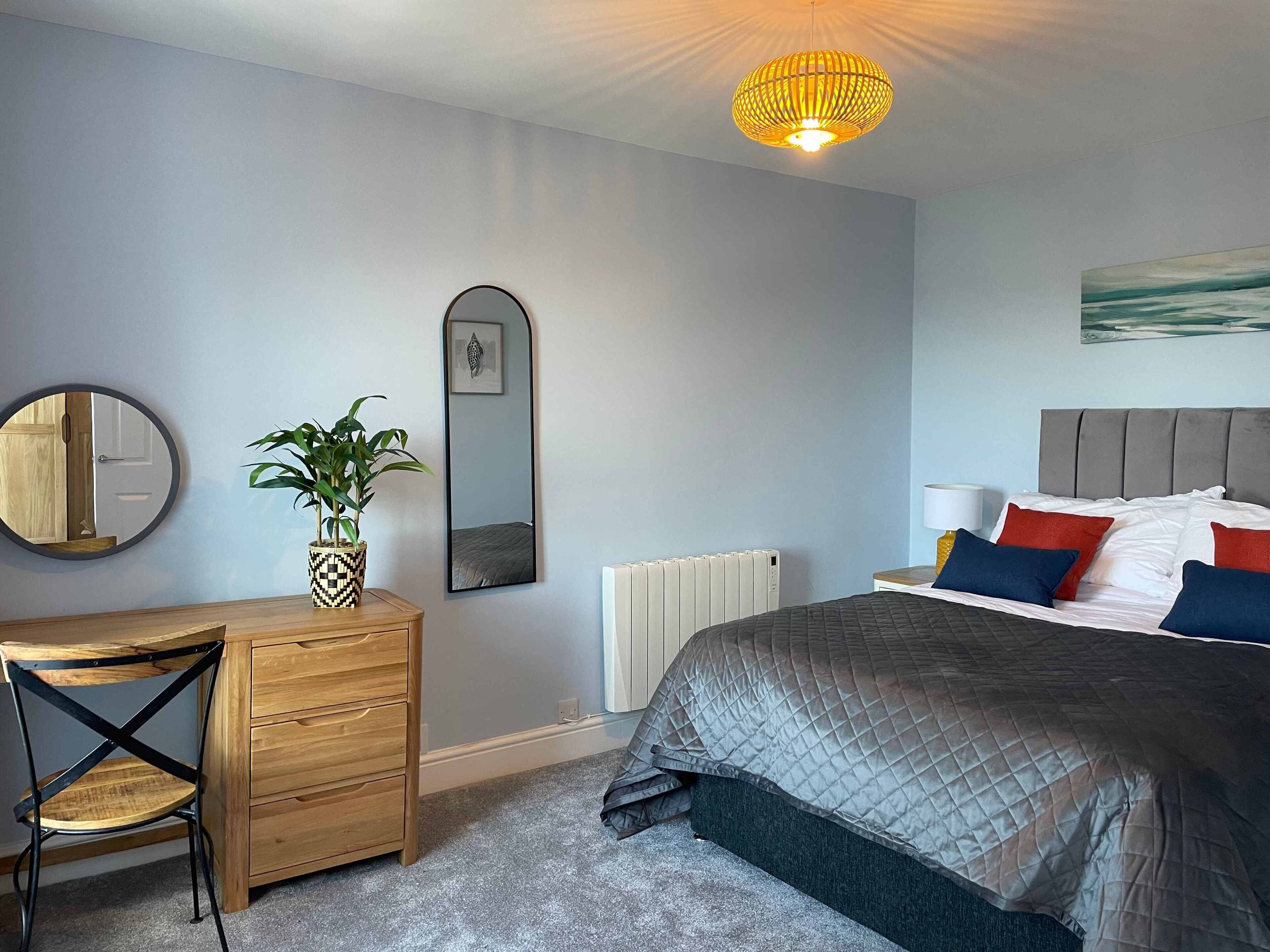 A bedroom with a bed, a desk, a chair, a mirror, and a radiator.