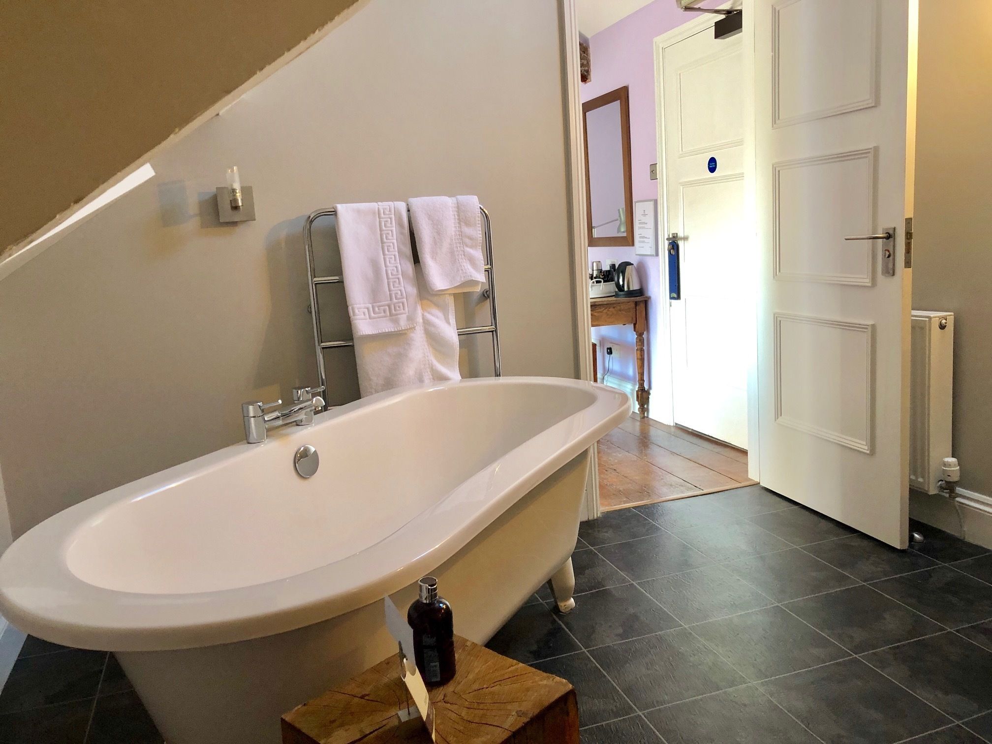 A bathroom with a freestanding bathtub, a wooden stool, and a towel rack with two towels.