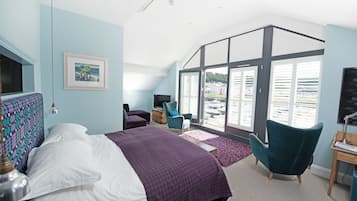 Un dormitorio con cama, escritorio, silla, televisor y una ventana grande con vistas a edificios.