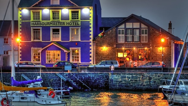 Hotel Harbourmaster con un cartel llamativo, un edificio de piedra con una tienda y barcos amarrados en el muelle.