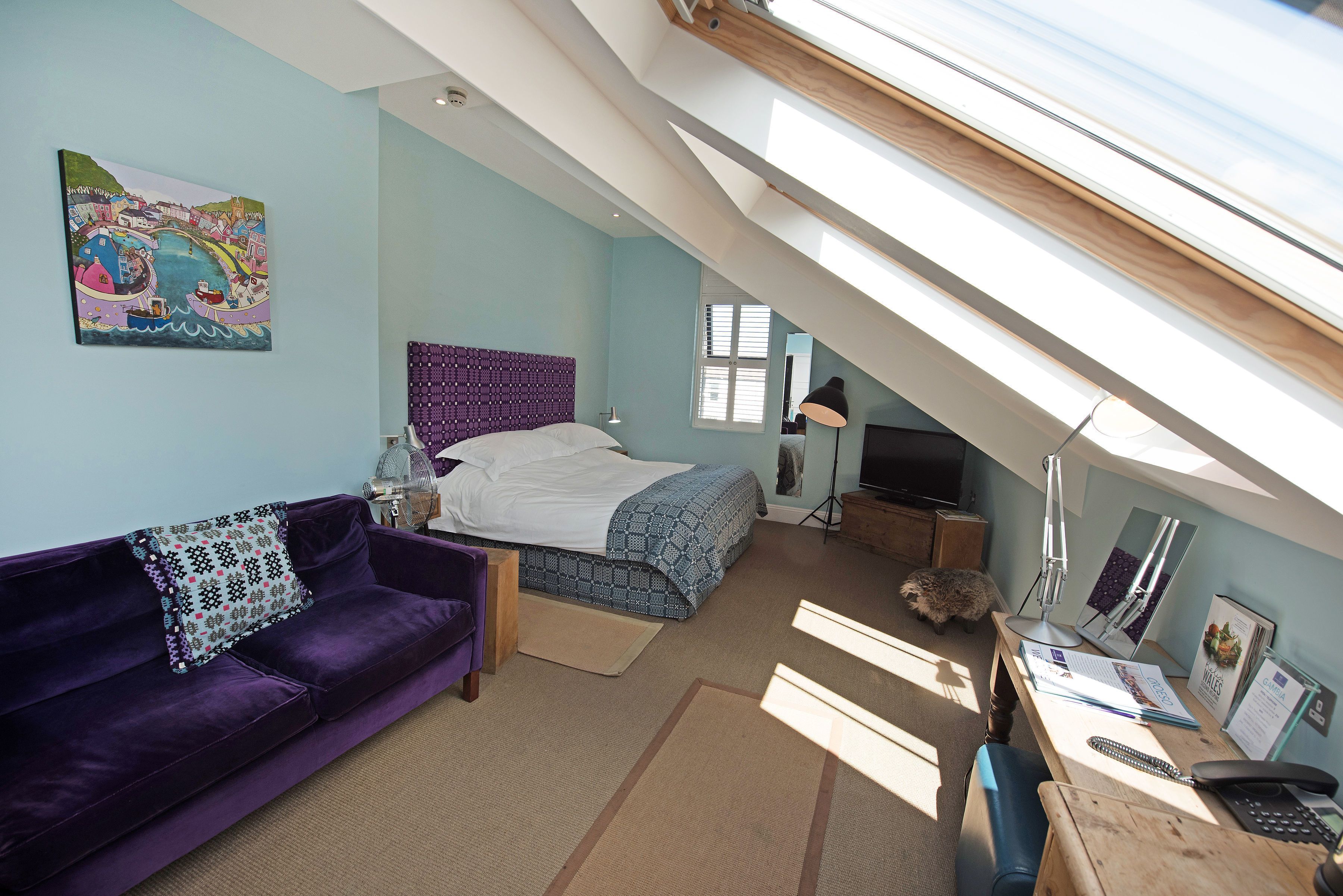 A bedroom with a bed, a purple sofa, a desk with a computer, and a painting on the wall.